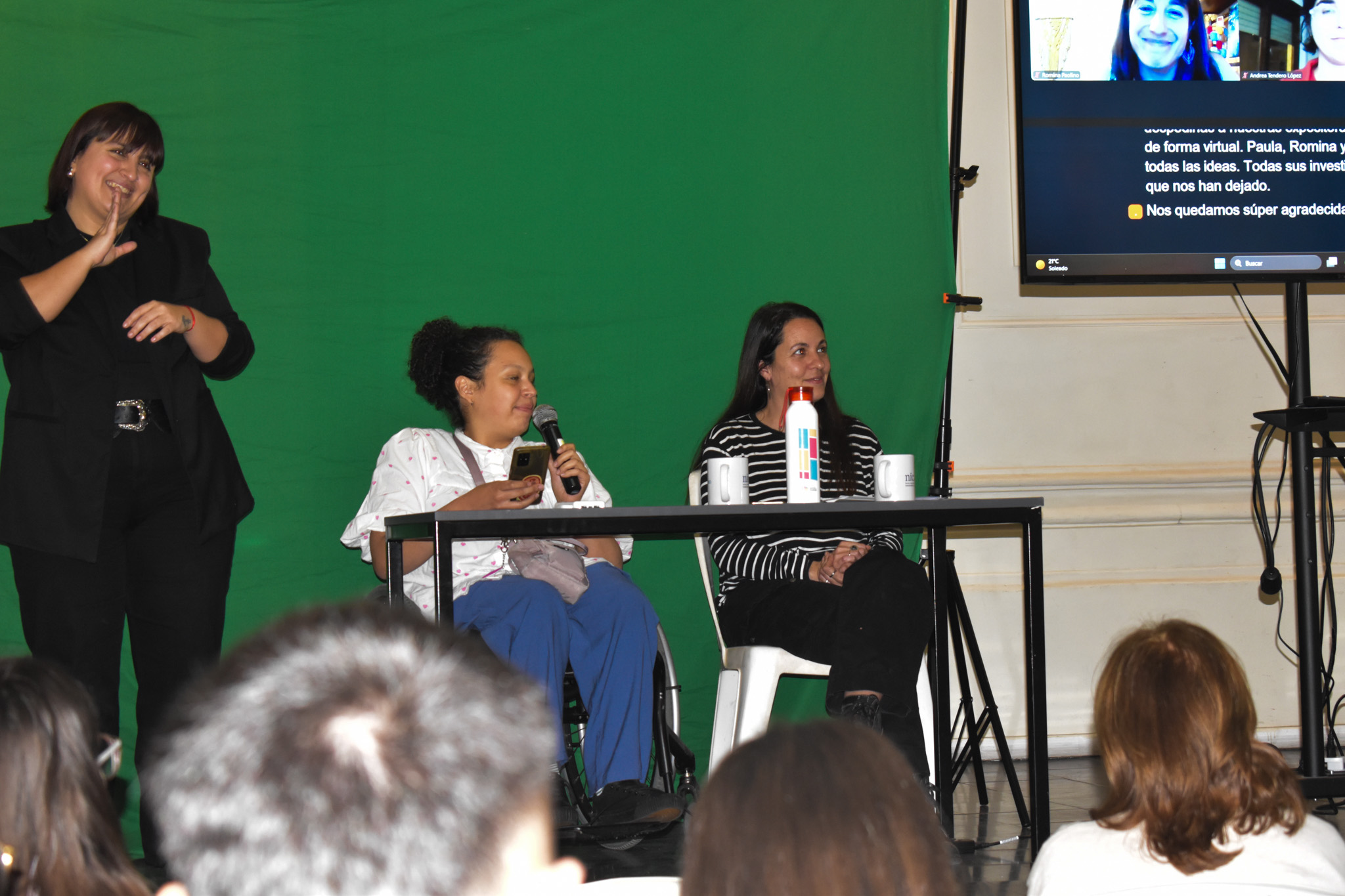 Una persona en silla de ruedas tiene un micrófono mientras habla. A su lado, una mujer de remera con rallas.